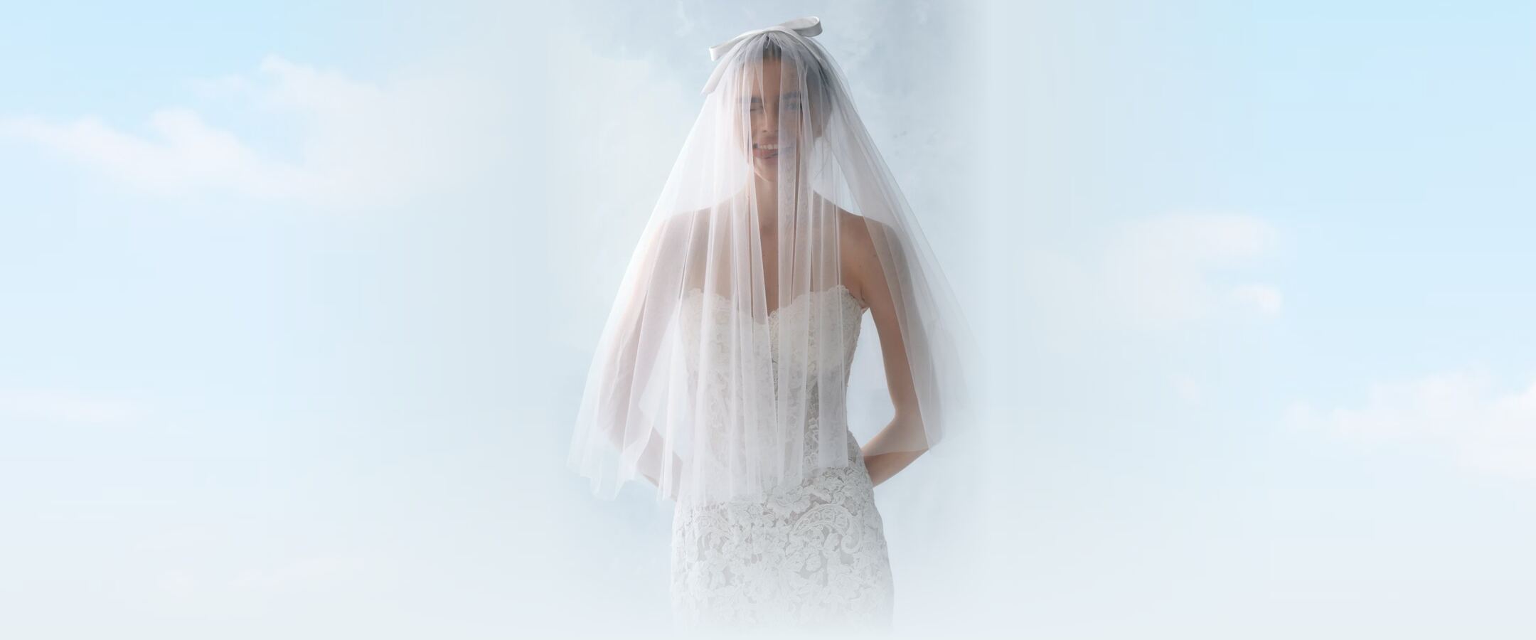 A smiling bride under a sheer veil tied with a satin bow