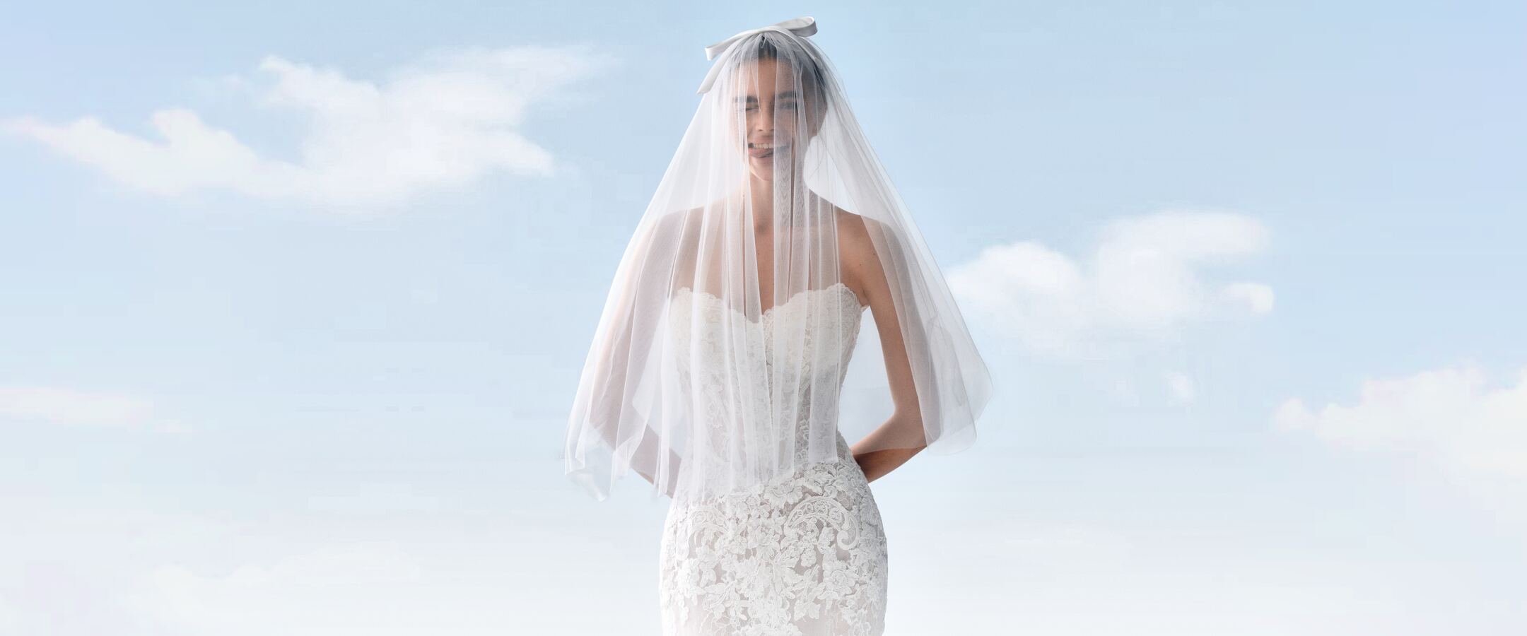 A smiling bride under a sheer veil tied with a satin bow