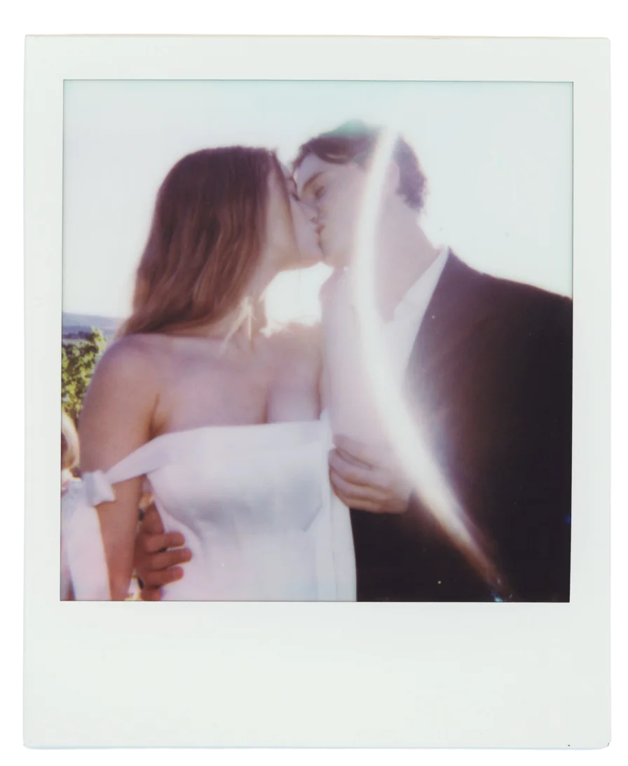 An instant photo of a bride and groom kissing in the sun